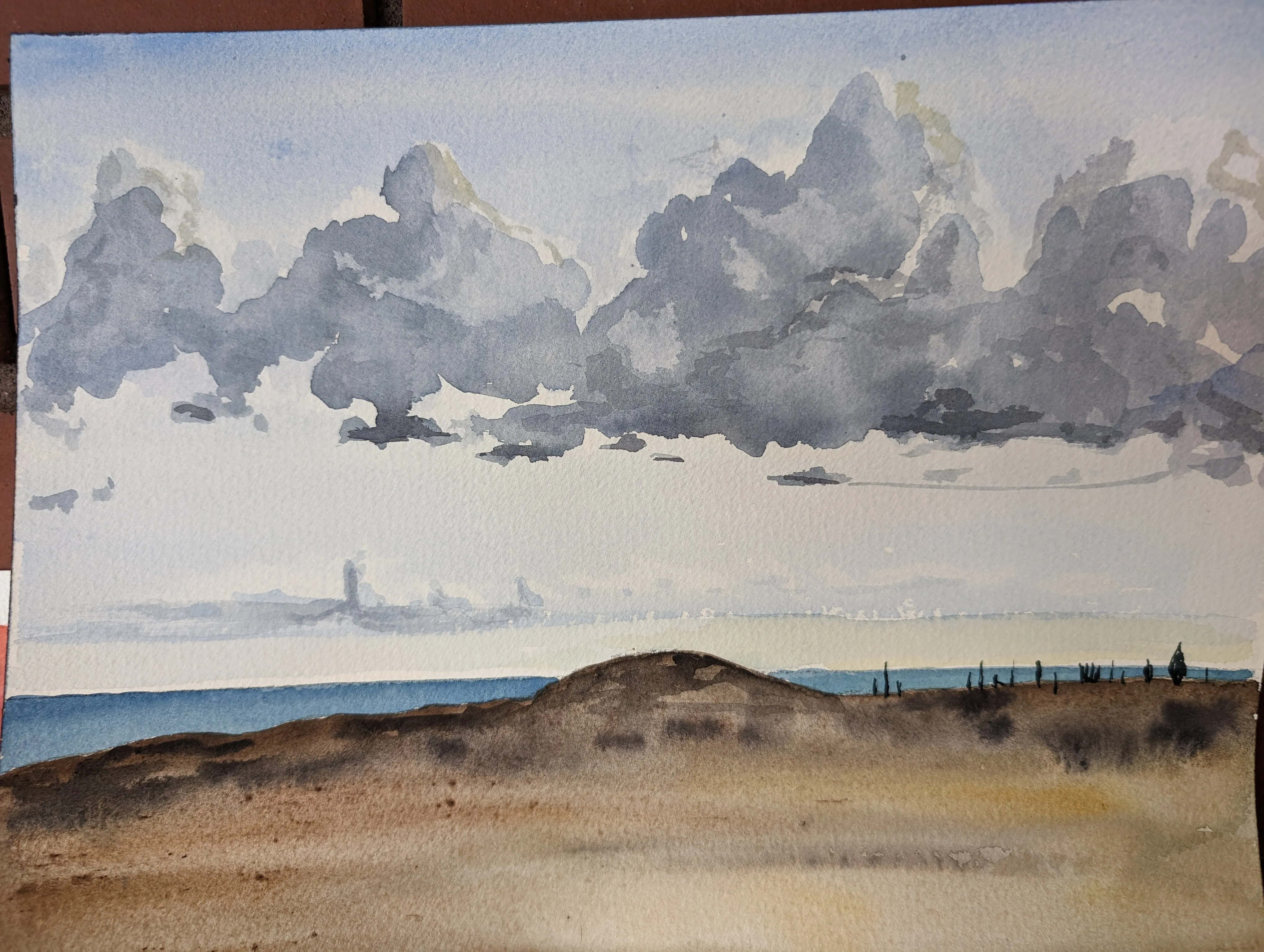 A watercolor of large gray clouds over a blue sea and a brown hillside.